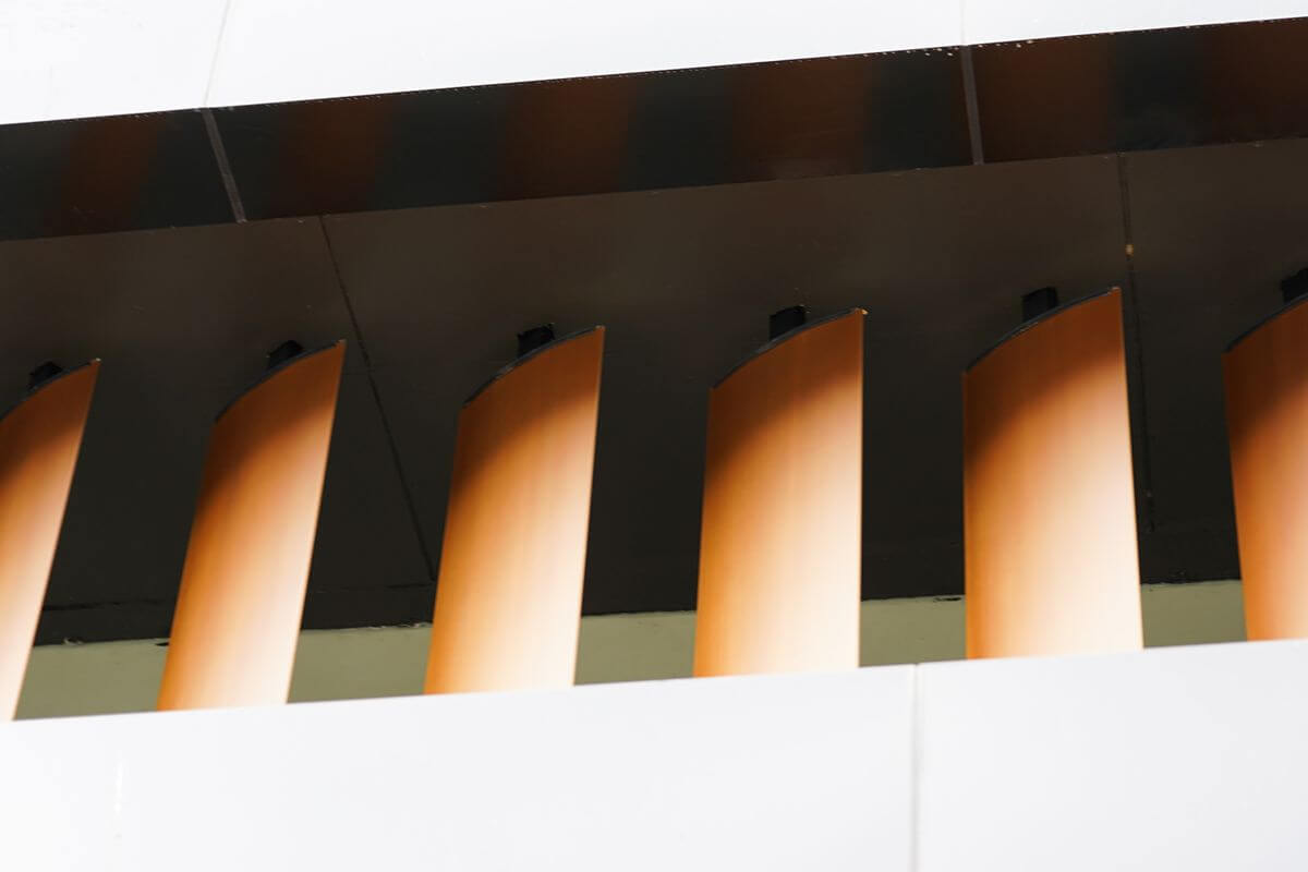 Curved wood-look facade fins beneath an exterior ceiling, showing architectural cladding detail on a modern building