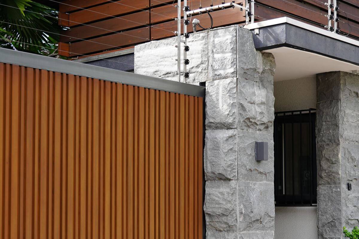 WPC wall cladding on a modern residential exterior with stone columns, balcony, and wood-look vertical panels